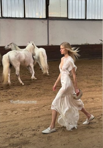 A model walks past a group of white horses.