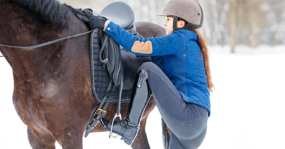 A woman mounting a horse in the snow.