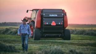 A man in a cowboy hat walking away from a large Kubota tractor.