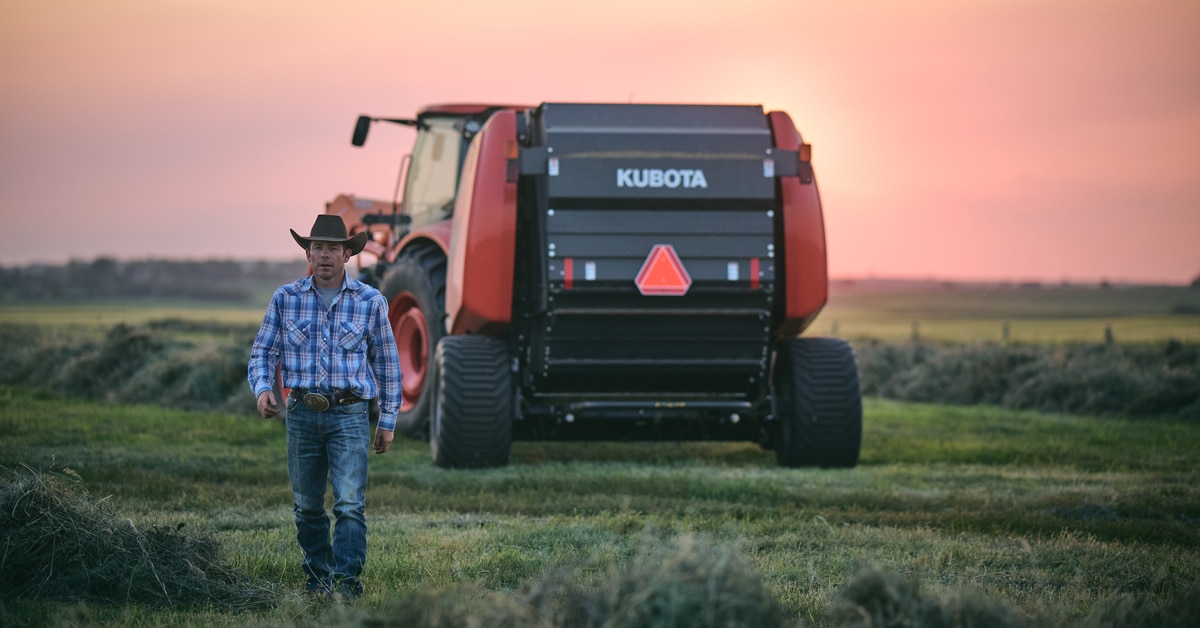 A man in a cowboy hat walking away from a large Kubota tractor.