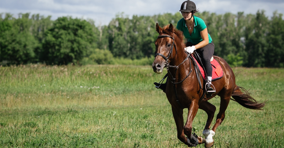 A young woman galloping a horse in a field.