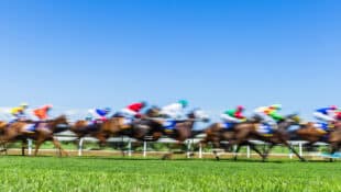 A blurred image of horses racing on a turf course.