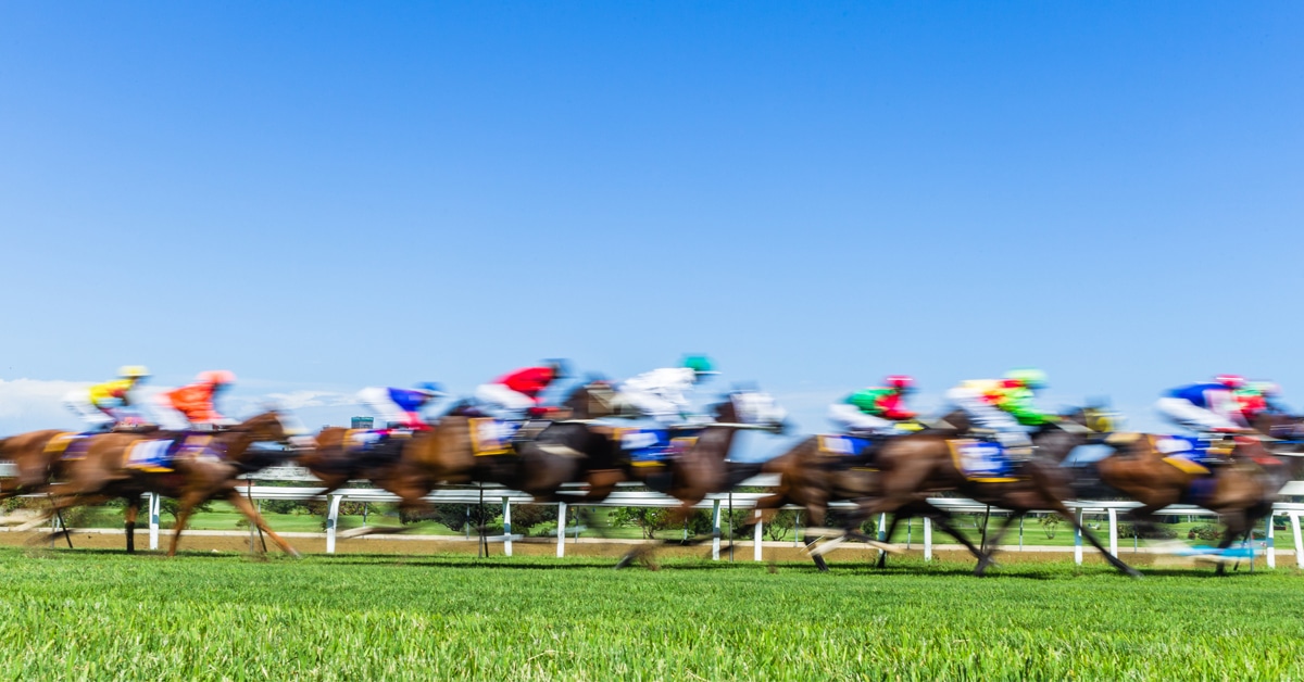 A blurred image of horses racing on a turf course.